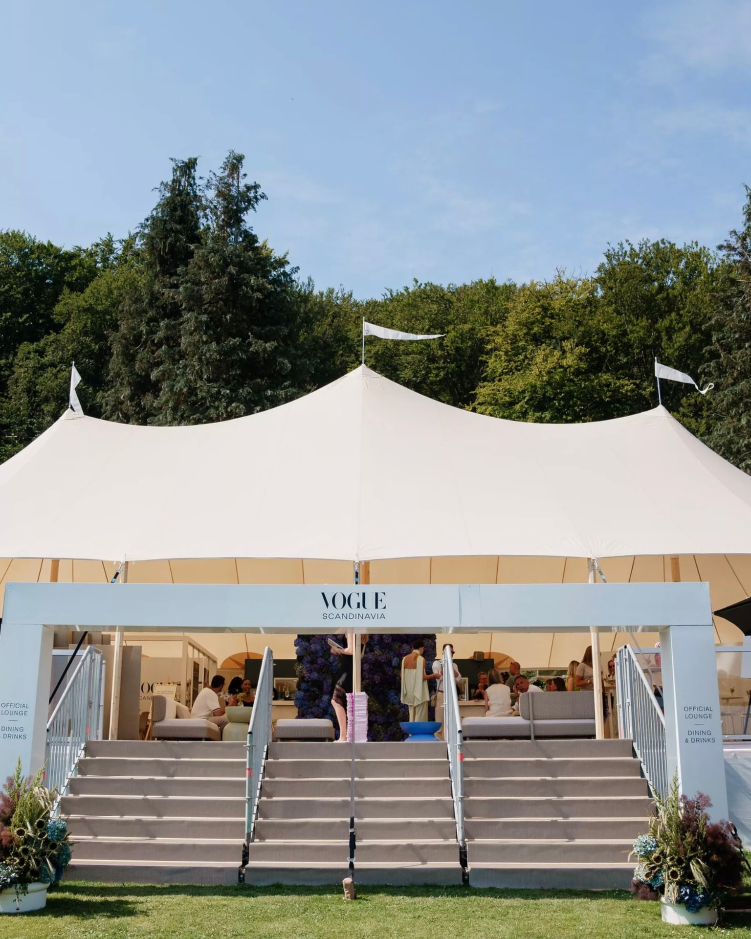 Vogue Scandinavia official lounge marquee with white sail tent and flower arrangements at an outdoor event