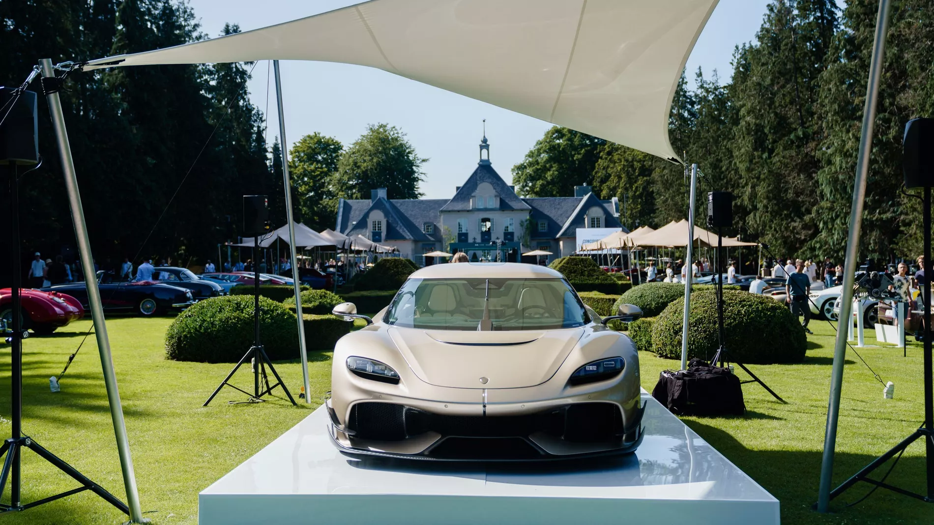Koenigsegg supercar on a white plinth under a shade sail at a concours event