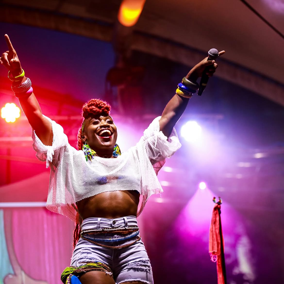 Performer on stage at LEAF Festival with arms raised under pink and purple lights