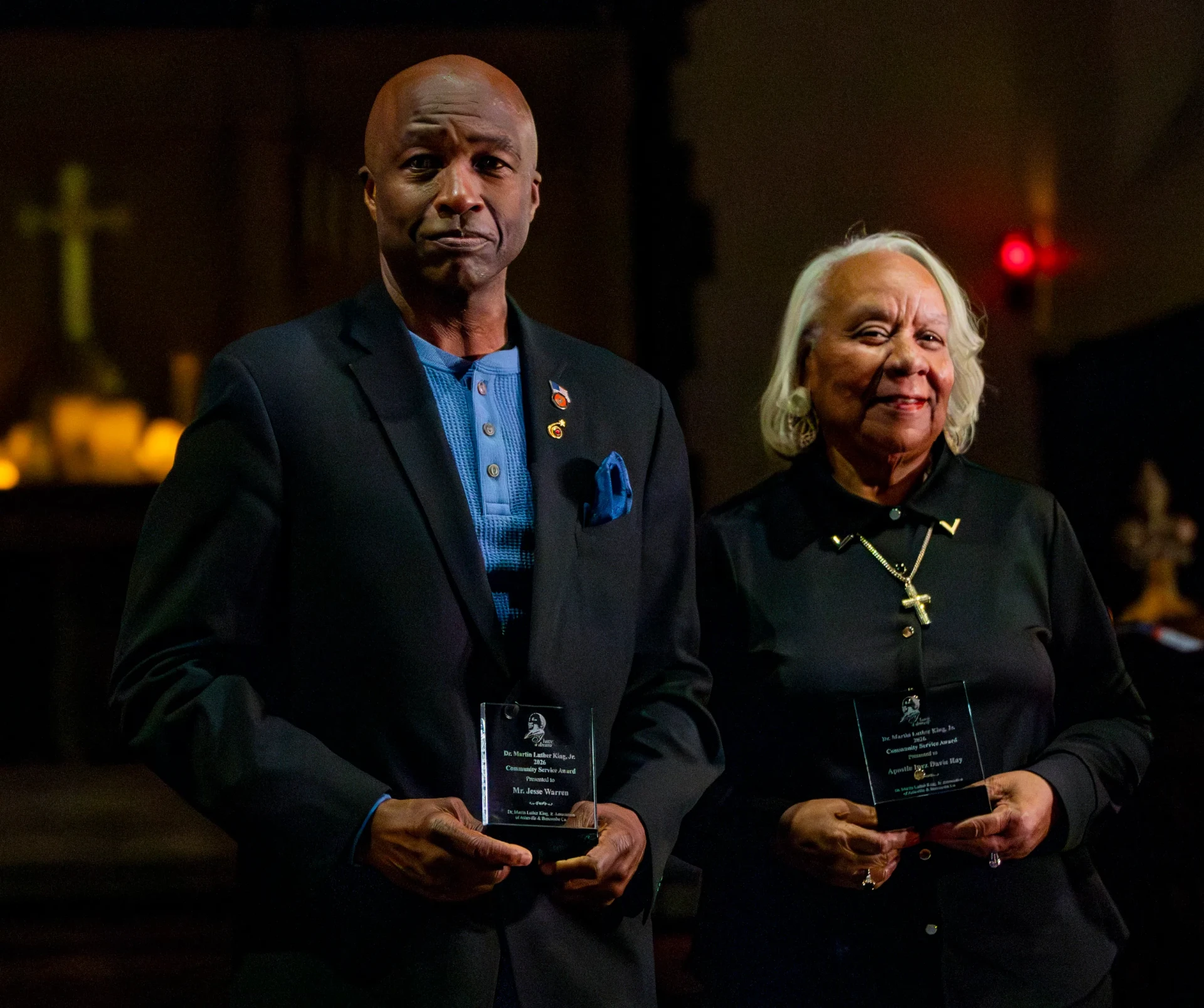 Two community service award recipients holding engraved glass awards at the MLK Candlelight Vigil
